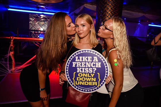 Hot women on Down Under party tour holding sign saying French kiss only down under in bedroom nightclub in Surfers Paradise